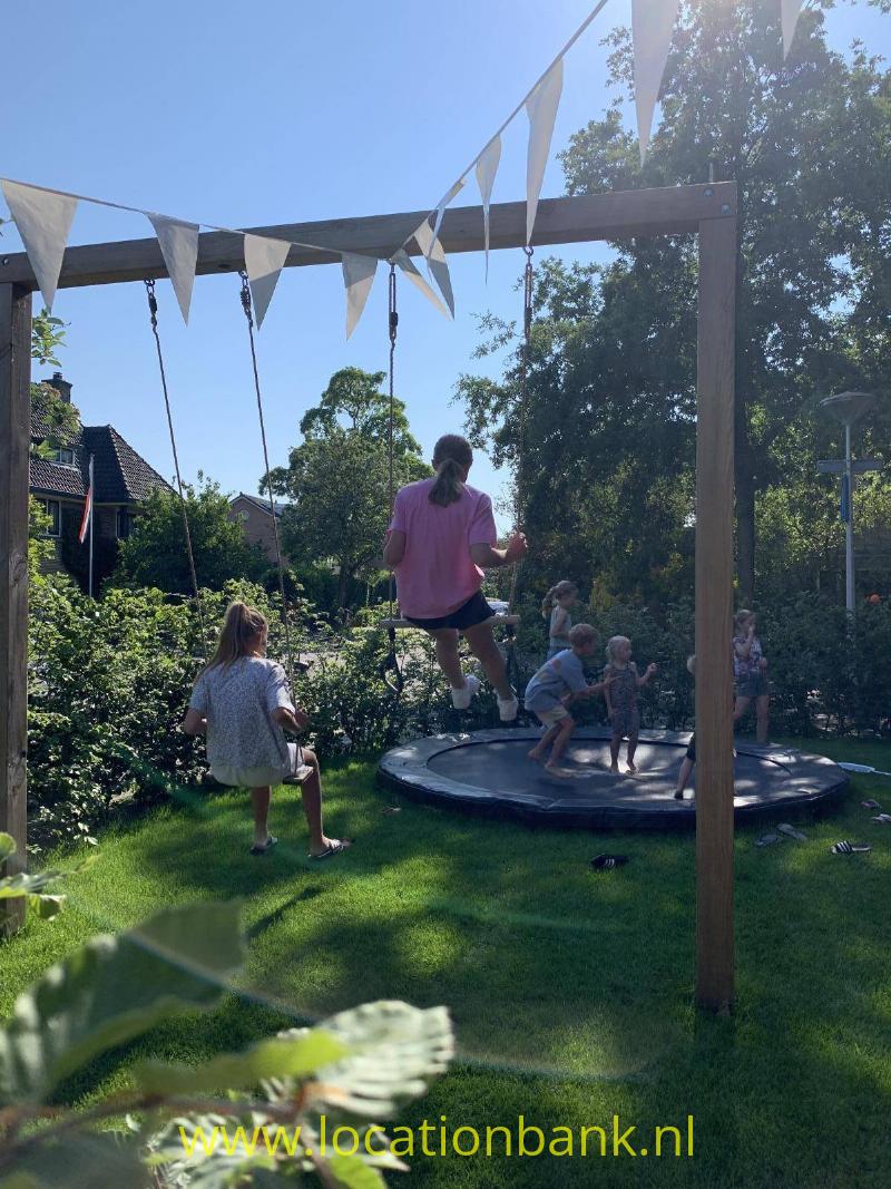 Tuin met schommel, en trampoline. Voorkant van het huis. 