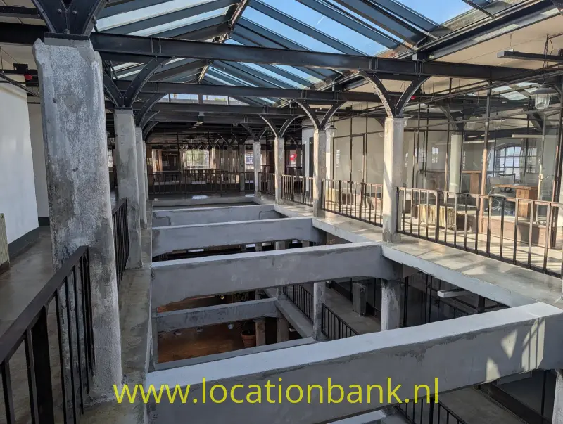 Meerdere galerijen met metalen balustrades omringen open verdiepingen onder een glazen dak.