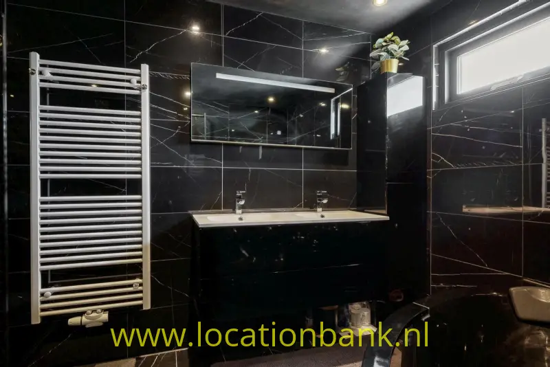 Badkamer met dubbele wastafel, zwarte marmerlooktegels, een spiegel en een witte handdoekradiator.