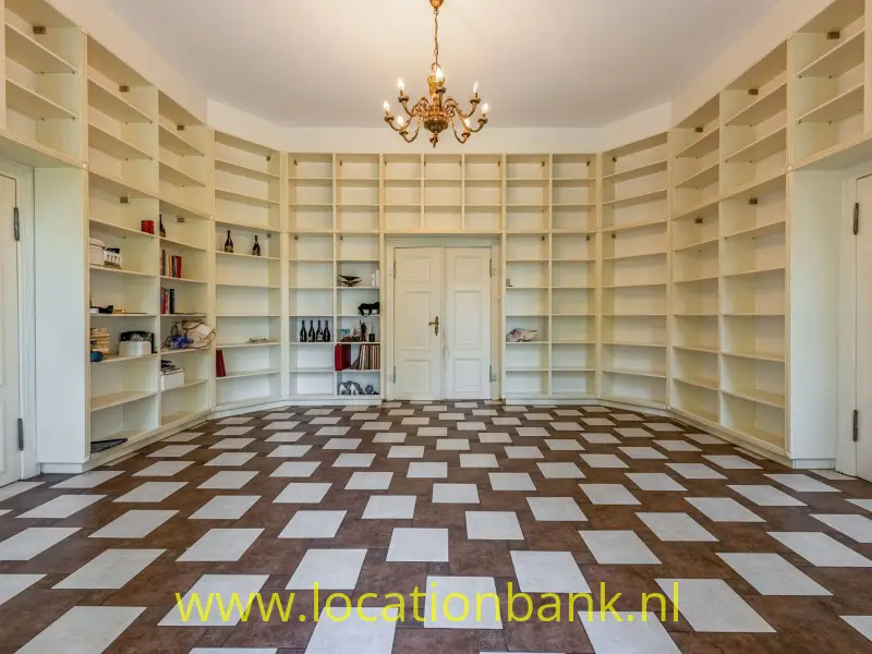 Karakteristieke bibliotheekkamer met kamerhoge witte boekenkasten, klassieke dubbele deuren en een opvallende vintage kroonluchter. Het bijzondere tegelpatroon en de symmetrische inrichting geven deze ruimte een authentieke, statige uitstraling. Ideaal als filmlocatie voor historische scènes, interieurfotografie en stijlvolle producties.
