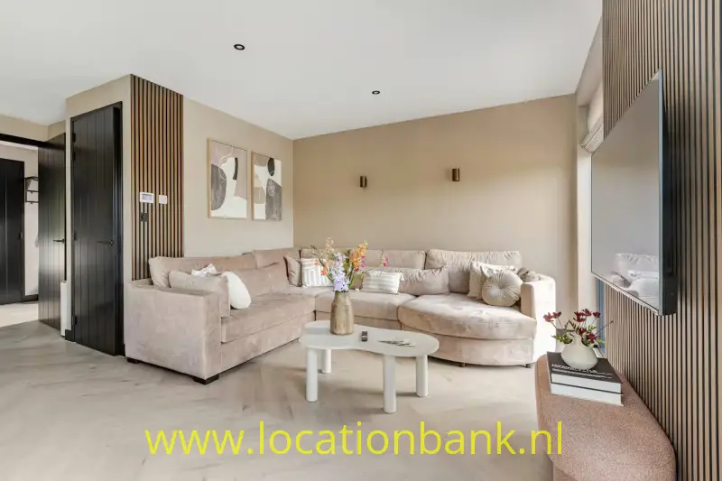 Woonkamer met twee beige zitbanken, een ovale salontafel en een wand met verticale houten latten.