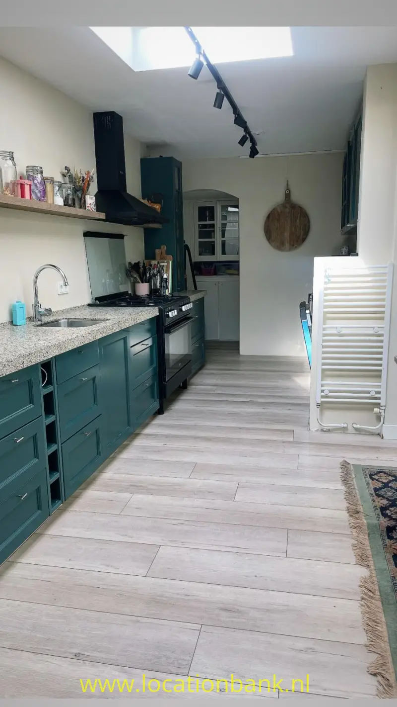 Donkergroene keuken met een gespikkeld werkblad, open plank, dakraam en witte handdoekradiator.