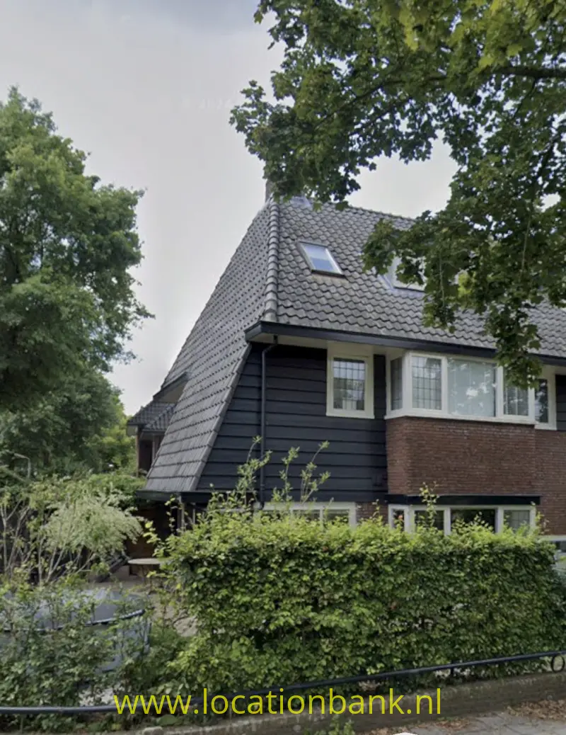 Dertiger jaren Huis met pannendak, donkere houten gevelbekleding, een bakstenen gevel en witte kozijnen.