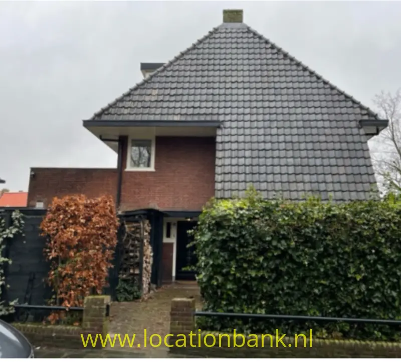 Vrijstaande woning met groot grijs pannendak, bakstenen gevel, voortuin en een overdekte entree.