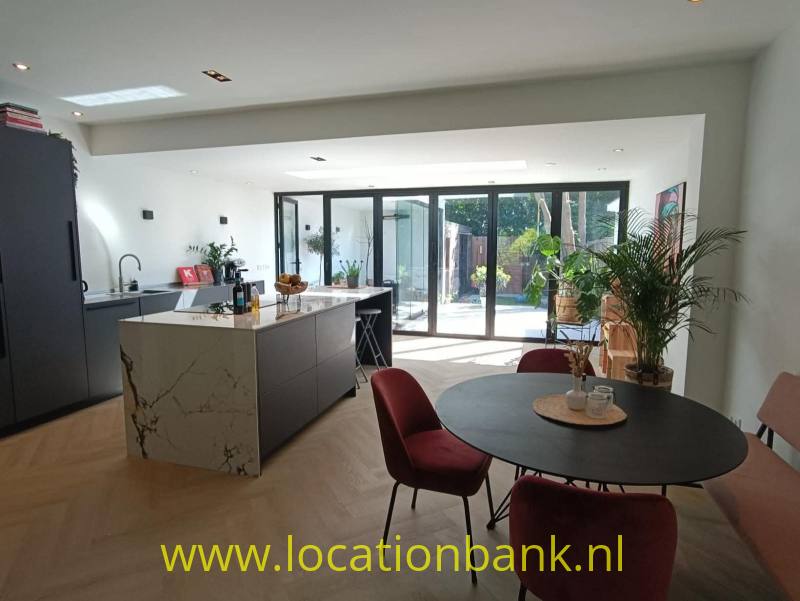 Open keuken met kookeiland en ronde eettafel bij glazen deuren naar een tuin.