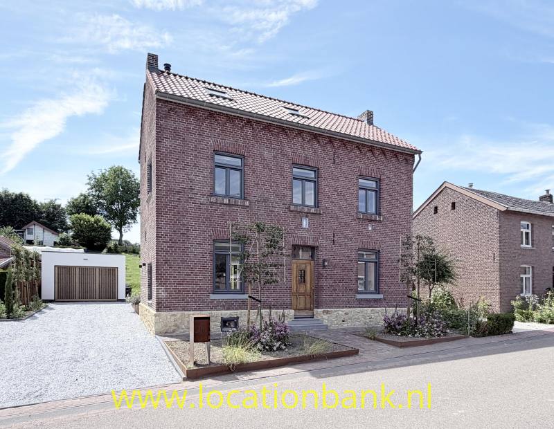 Voorzijde van huis in Rode bakstenen huis met twee verdiepingen, een zadeldak, houten voordeur en vrijstaande garage.