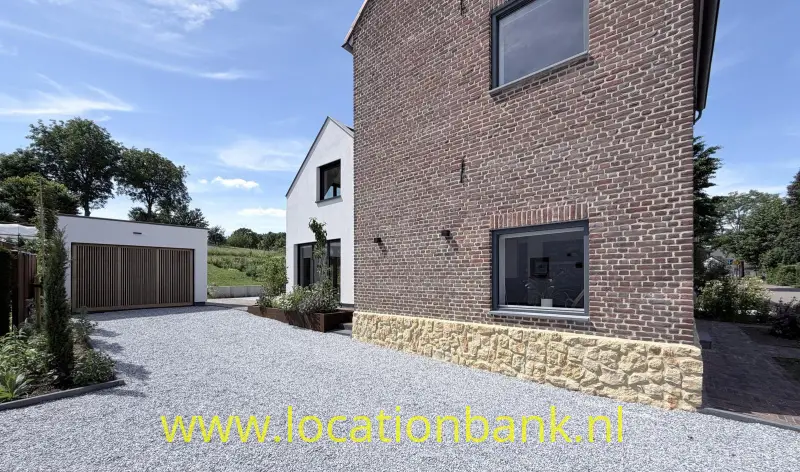 Bakstenen woning met een natuurstenen plint, een grindoprit en een vrijstaande garage.
