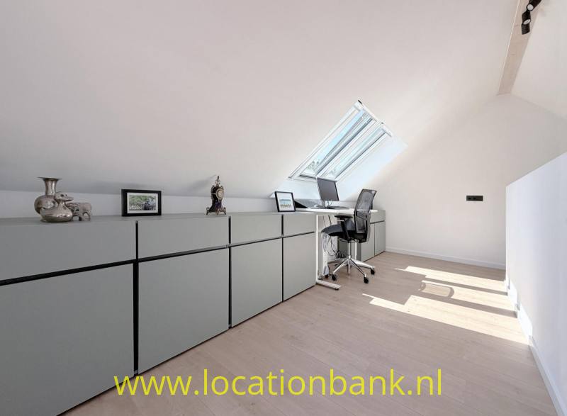 Lange lage kastenwand in een lichte zolderruimte met een dakraam, bureau en bureaustoel.