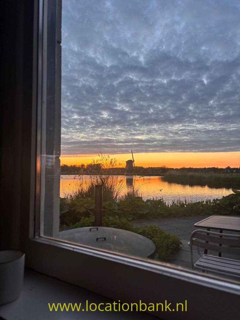 Een met riet omzoomd meer weerspiegelt de oranje zonsondergang, gezien door een raam.