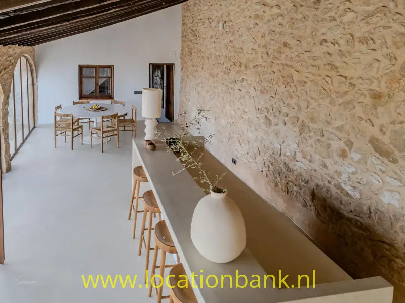 Lange toonbank met barkrukken en witte vazen langs een ruwe stenen muur.