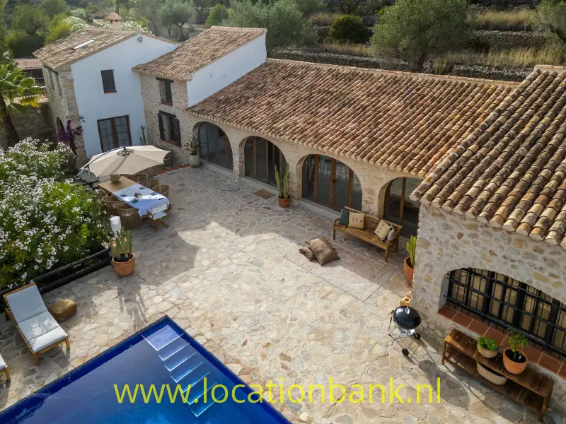 Binnenplaats met natuurstenen bestrating, terracotta dakpannen, een blauw zwembad en een overdekte galerij.