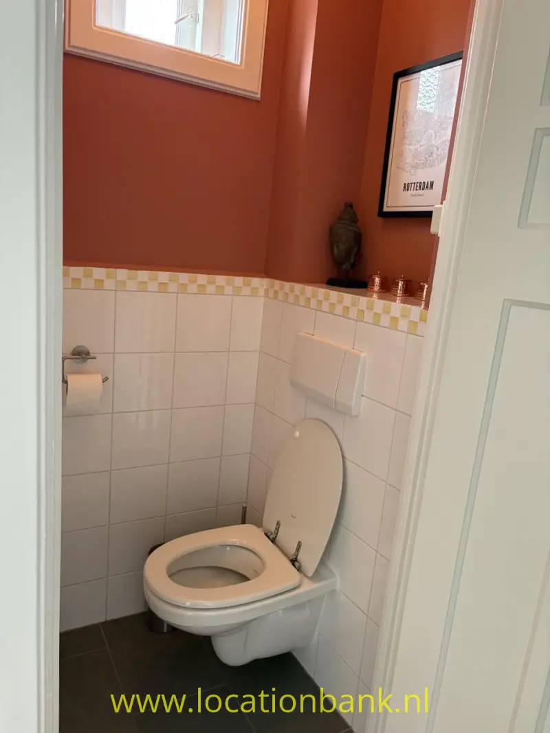 Toilet met witte betegelde wanden, een decoratieve tegelrand, donkere vloertegels en terracottakleurige muren.