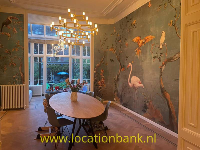 Eetkamer met een ovale houten tafel, een kroonluchter en behang met vogelmotieven.