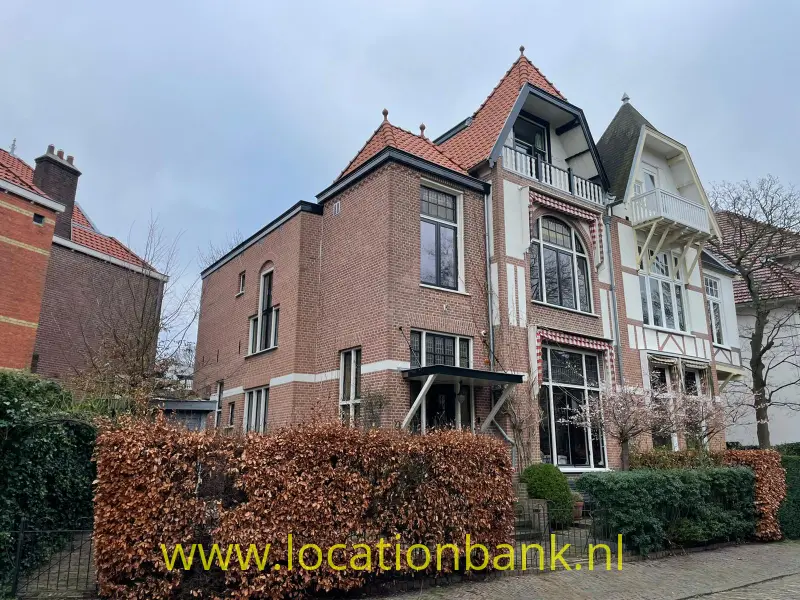 Aaneengeschakelde bakstenen woningen met rode pannendaken en een wit gedetailleerde gevel achter heggen.