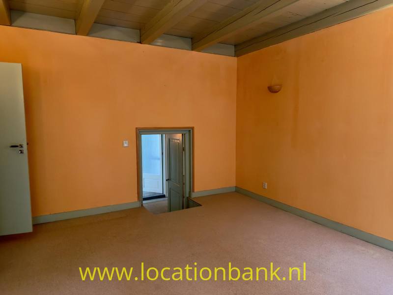 Lege kamer met oranje pastel muren, een houten plafond, een deur en een laag geplaatst raam.