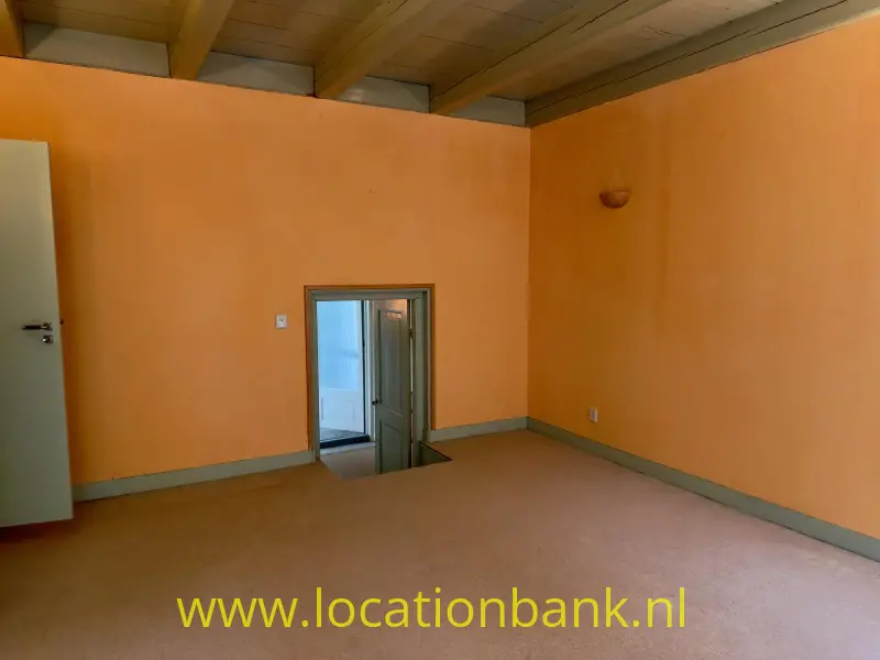 Lege kamer met oranje pastel muren, een houten plafond, een deur en een laag geplaatst raam.