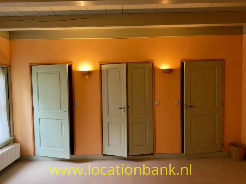 Oranje kamerwand met meerdere lichtgekleurde groene deuren.