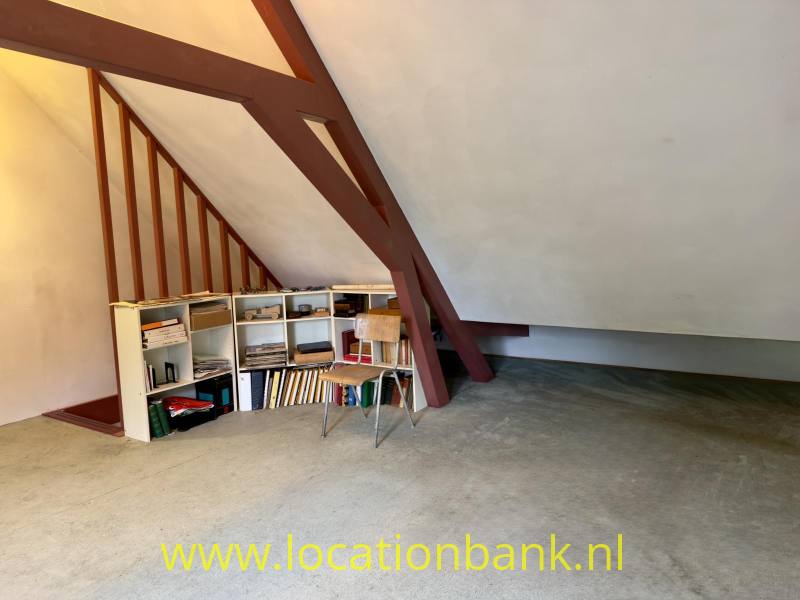 Houten dakspanten en open opbergkasten staan in een zolderruimte met een lage schuine kap.