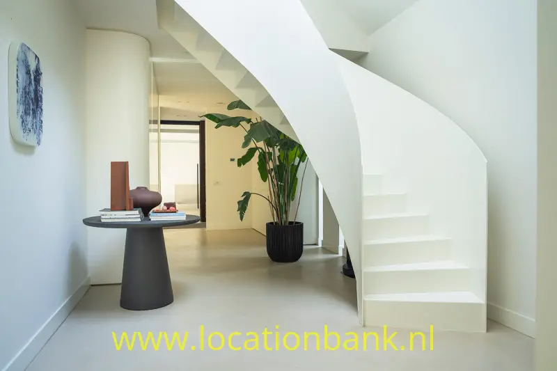 Witte, gebogen trap met open treden naast een ronde tafel en een grote kamerplant.