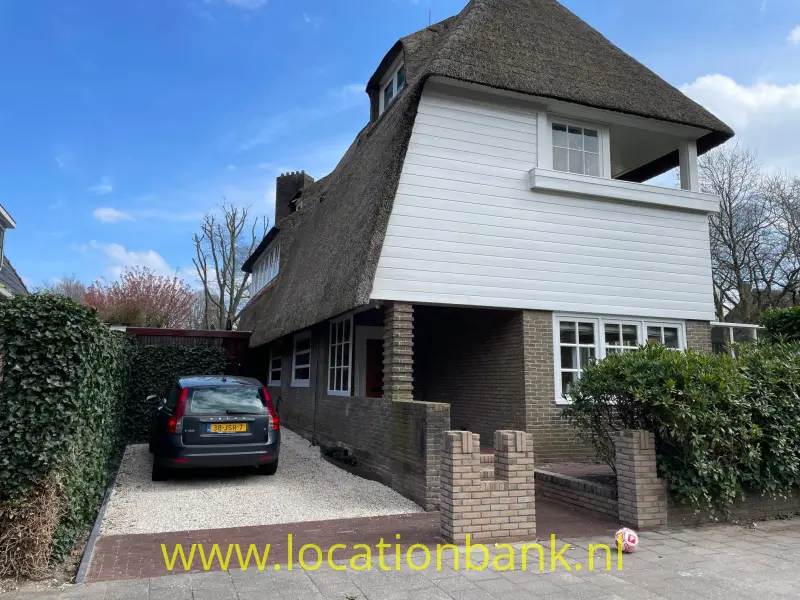 Vrijstaand huis met rieten dak, witte gevelbekleding, bakstenen onderbouw en een auto op de oprit.