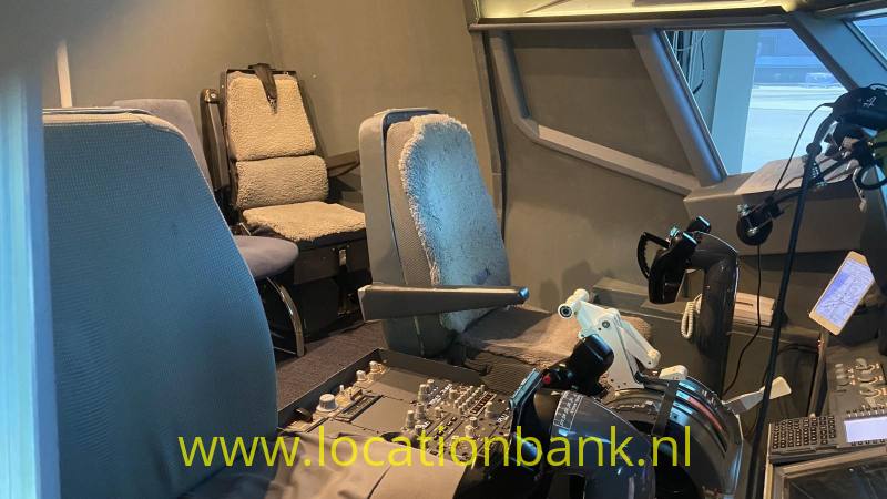 Cockpit met meerdere stoelen, bedieningspanelen, stuurknuppels en grote ramen