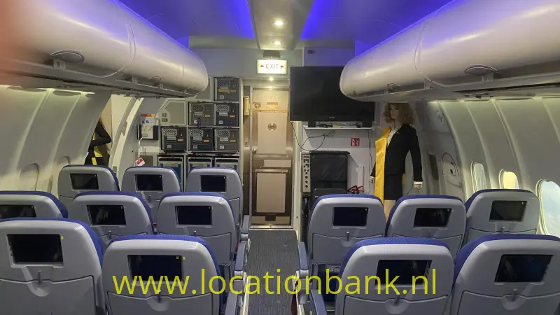 Rijen passagiersstoelen met schermen staan in een vliegtuigcabine met blauwe plafondverlichting.
