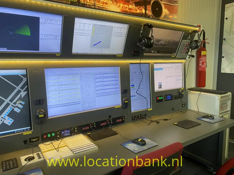Bedieningsconsole met meerdere computerschermen, technische apparatuur, verlichte panelen en een rode brandblusser.
