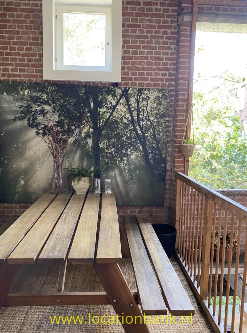 Een houten picknicktafel met banken staat tegen een bakstenen muur naast een houten balustrade.