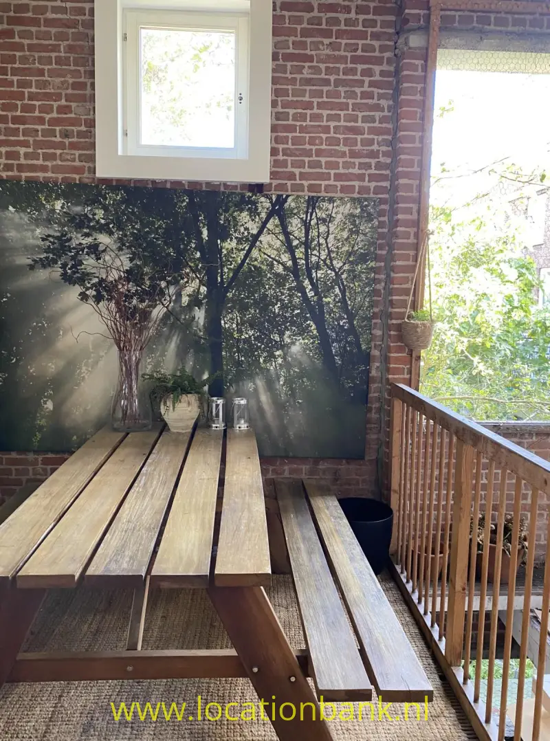 Een houten picknicktafel met banken staat tegen een bakstenen muur naast een houten balustrade.