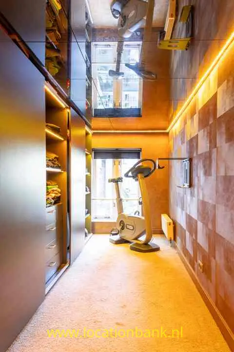 Een hometrainer staat in een smalle ruimte met een spiegelplafond, ingebouwde kasten en warme verlichting.