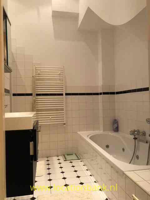 Een betegelde badkamer met een ligbad, een witte handdoekradiator en een zwart badkamermeubel.