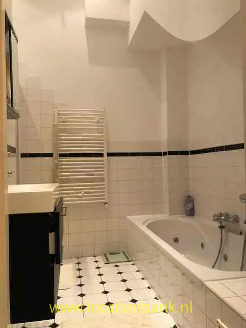 Een betegelde badkamer met een ligbad, een witte handdoekradiator en een zwart badkamermeubel.