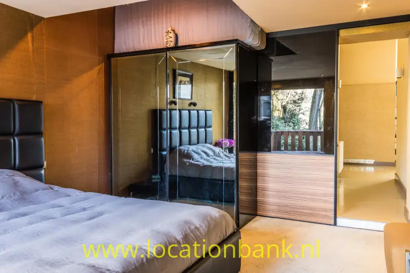 Slaapkamer met een groot bed, een glazen kast en een open doorgang naar een balkon.