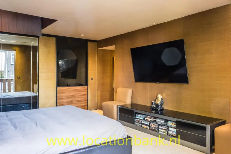 Slaapkamer met een groot bed, een aan de wand gemonteerde televisie en een laag donker meubel.
