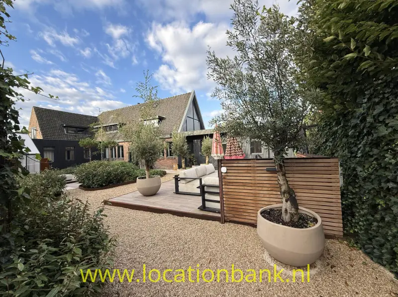 Houten terras met zitmeubels, plantenbakken en een groene tuin voor een huis met een puntdak.