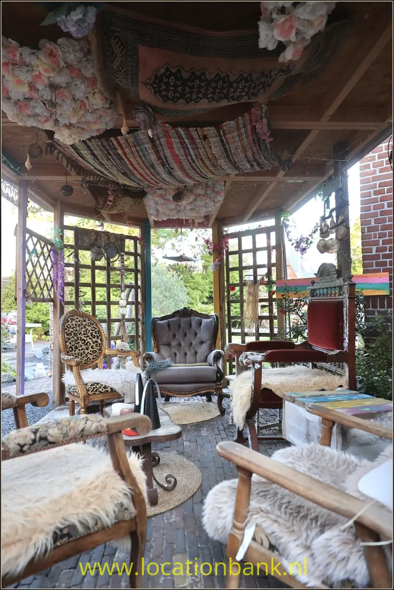 Overdekte zithoek in serre met fauteuils met pluizige bekleding, kleurrijke hangende stoffen en een bakstenen vloer.