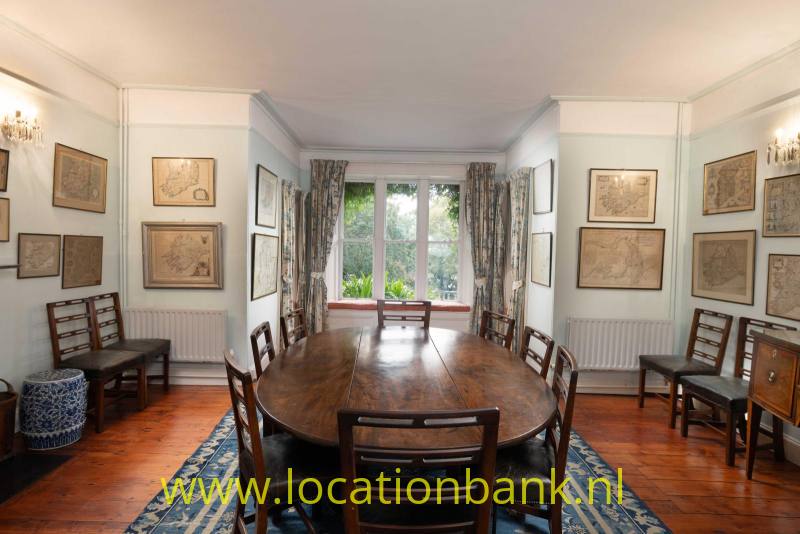 Klassieke Eetkamer met een lange ovale houten tafel met stoelen staat voor een raam, omringd door ingelijste kunstwerken.