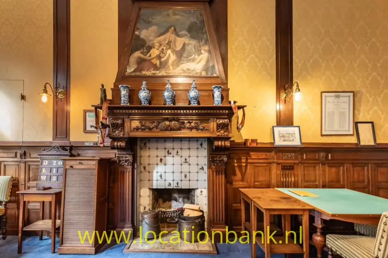 Een open haard met betegelde ombouw, een schilderij erboven en houten lambrisering rondom.