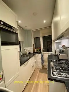 Witte keuken met zwarte werkbladen, een ingebouwde oven, een gasfornuis en een raam aan het einde.