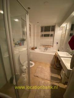 Badkamer met een ligbad onder het raam, een glazen douchecabine, een toilet en een wastafel.
