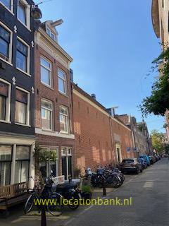 Bakstenen gevels langs een smalle straat met geparkeerde fietsen en bomen onder een heldere blauwe lucht.