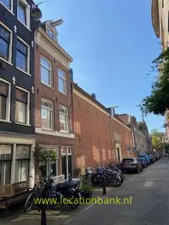 Bakstenen gevels langs een smalle straat met geparkeerde fietsen en bomen onder een heldere blauwe lucht.