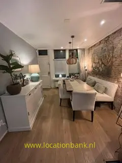 Eetkamer met een lange houten tafel, gestoffeerde stoelen en een bakstenen wand met een grote muurschildering.