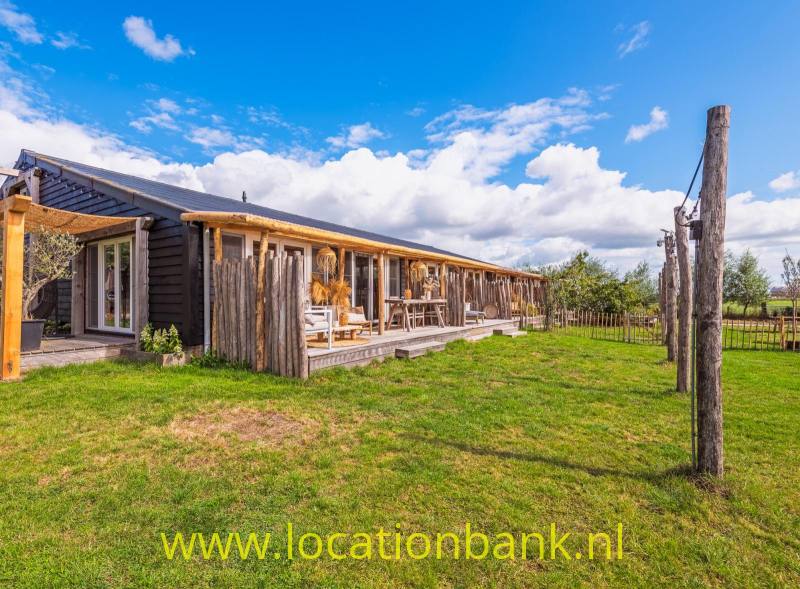 Lang, laag houten gebouw met een overdekte veranda, grasveld en houten omheining.