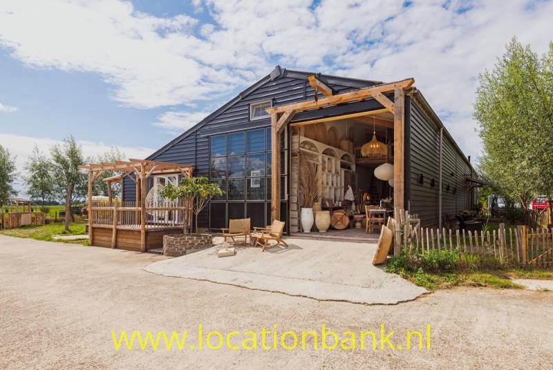 Donker houten stal met een grote glazen gevel, open entree en houten pergola aan de voorkant.