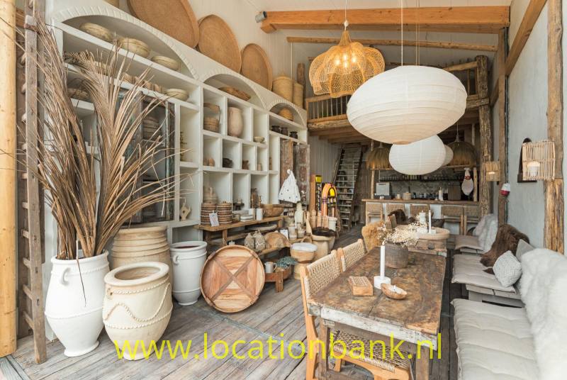 Interieur met open houten schappen, aardewerken potten, gedroogde takken, een houten tafel en hangende lampen.
