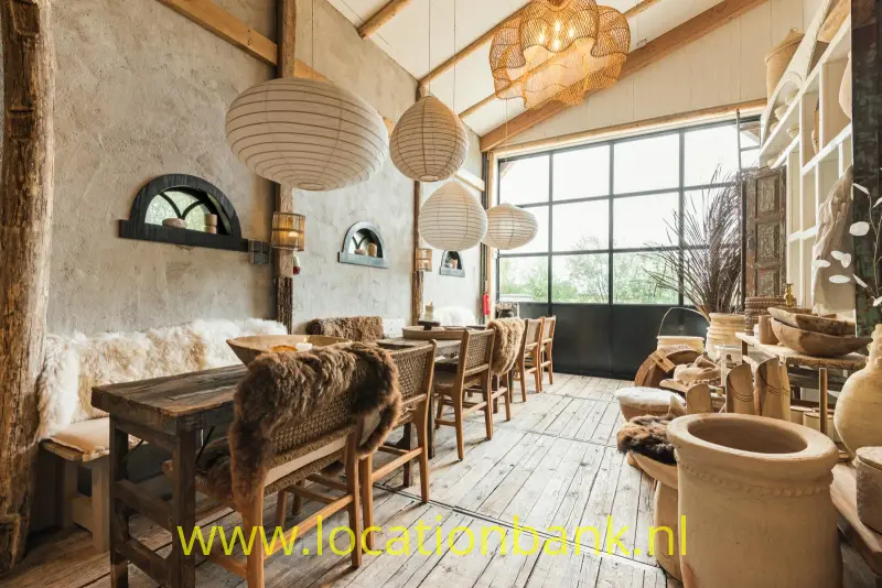 Lange houten tafel met stoelen, hanglampen, een grote raampartij en vachtjes in een lichte ruimte.