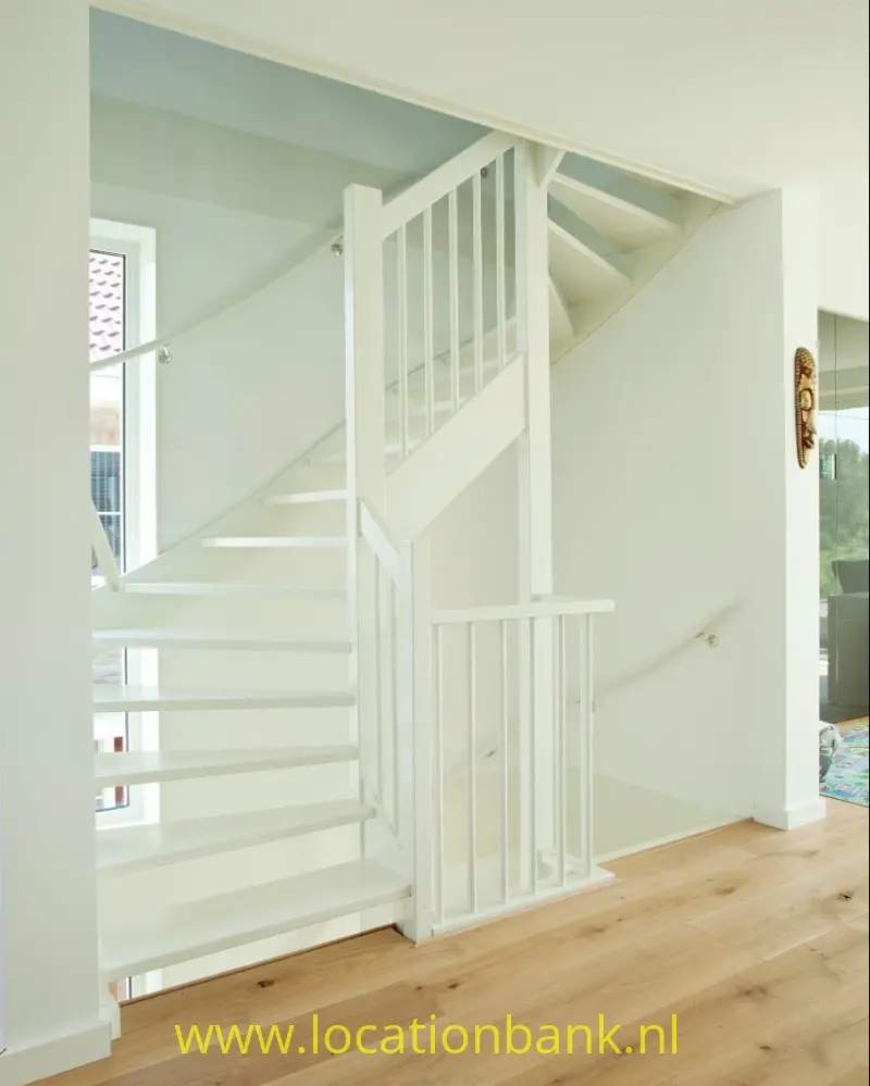 Witte trap met open treden en verticale spijlen loopt vanaf een houten vloer naar boven.