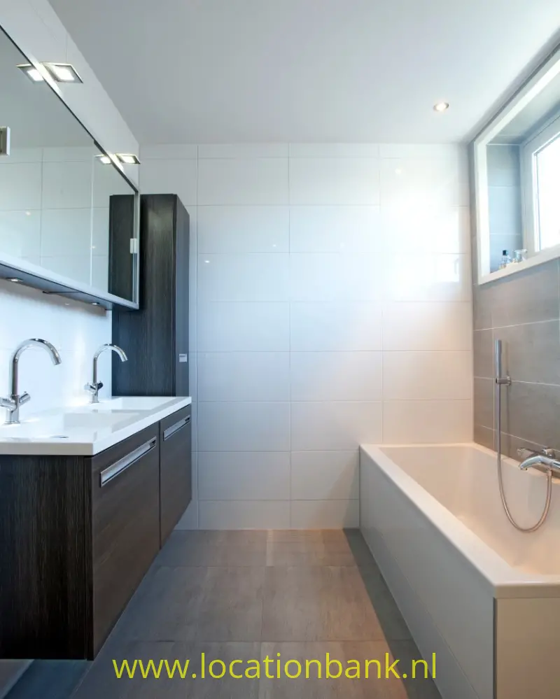 Badkamer met dubbele wastafel, donkere onderkasten, witte wandtegels en een ligbad bij het raam.