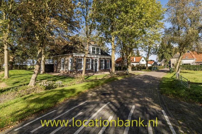 Gekasseide oprit met witte markeringen langs een vrijstaand gebouw tussen bomen en gras.